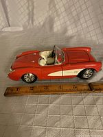 Side view of 1957 Corvette diecast model in red with white side panel, showing details including interior and rims. Scale shows about 7 inches long.