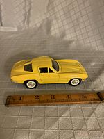 Yellow 1963 Chevrolet Corvette diecast model measured next to a ruler showing approximately 5.5 inches in length, displayed closed.