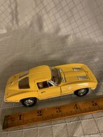 Yellow diecast model of 1963 Corvette measured against ruler showing approx 5.5 inches length and 2.5 inches width.