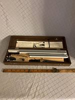 Open wooden box with multiple stacked metal alphabet lettering plates and tools inside, ruler below for scale.