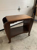 Side view of the antique Art Deco style wooden magazine table showing curved legs and open shelf.
