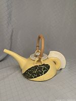 Side view of yellow raku-fired teapot with crackle black patch and woven handle