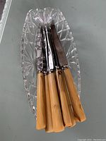 Seven cutting knives with tan Bakelite handles inside a clear depression glass pickle dish.