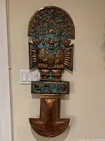 Full view of the Fearless Inca Tumi copper wall art showing its intricate embossed design and coloration with patina against a wall.