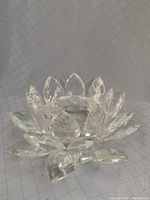 Clear crystal lotus flower-shaped candle holder with multi-faceted petals resting on a fabric surface.
