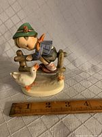 Front view of Hummel Goebel figurine showing boy with goose in front of fence, ruler for scale.
