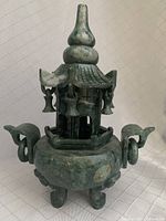 Full view of the jade incense pot with lid on, showing the pagoda-style top with hanging bell decorations and the rounded base with side handles and tripod legs.