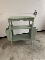 Front view of the distressed mint green magazine table showing two shelves and side magazine compartments.