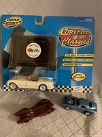 Photo showing three Corvette die-cast model cars, including one in original packaging labeled Corvette Classics 1953 Corvette Roadster with collectible license plate and two unpackaged die-cast models: brown streamlined and blue coupe.