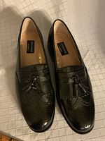Top view of the pair of black leather tassel loafers showing brogue perforation details and tassels on each shoe.