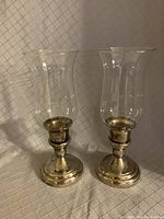 Two silverplated candle holders with glass chimneys placed upright, showing overall form and style.