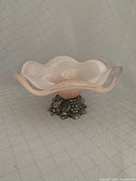 Side angle showing the translucent ruffled edge bowl with pink center and decorative metal floral base