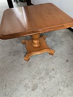 Full view of the solid oak end table showing square top and pedestal base on concrete floor.