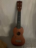 Front view of wooden ukulele showing missing one string and fretboard with dot inlays.