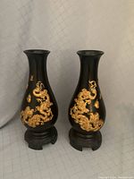 Front view of both black Bakelite vases showing detailed gold dragon designs and wooden stands.