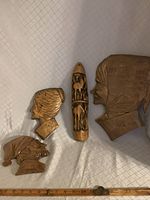 Four vintage wood carvings displayed on a fabric surface with a measuring tape showing their dimensions; three profile wall hangings and one 3D antelope carving