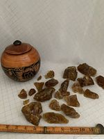 Wooden jar next to multiple amber fire glass stones scattered on surface with measuring ruler for scale.