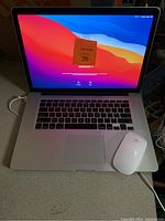 Apple MacBook laptop screen and keyboard powered on with Apple Magic Mouse beside it