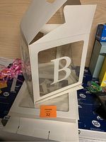 Photos of white decorative baby boxes with transparent sides and letter B on them.