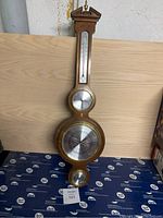 Full view of vertical wooden weather station featuring barometer, clock, and small bottom gauge