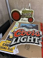 Four beer signs and a vintage mountain landscape picture shown on a cardboard box in a concrete corner.