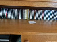 Wide shot of a wooden shelf containing approximately 38 assorted music CDs arranged side by side with visible spines.