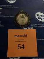 Photo of the commemorative coin pendant showing the front side of the coin with leaf motif metal border.