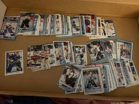 Multiple stacks of assorted hockey goalie trading cards from various sets and years, arranged in a cardboard box.