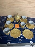 Full set showing 6 teacups with gold handles placed on leaf-shaped saucers, arranged with a lidded sugar bowl in the center.