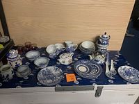 Wide view showing entire lot arranged on table with multiple porcelain tea set pieces in blue and white as well as glass cups.