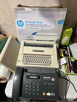 Photo showing Brother fax phone machine, electric typewriter, HP DeskJet 3632 printer box, and some office supplies on a table.