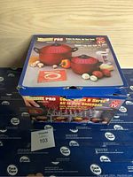 Photo of Pasta Pro Original product box showing the image of the red all-in-one pasta cooker, some mushrooms, potatoes and a glass of wine beside the pot as decoration to indicate cooking.
