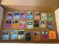 Pokémon cards arranged in neat rows inside a cardboard box, showing various Pokémon with some holo and reverse holo patterns.