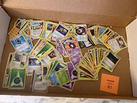 Wide view of numerous Pokémon cards spread out in a box, showing a variety of card types and colors including energy and character cards.