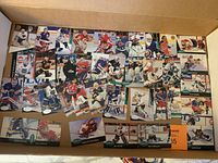 Photo showing a wide spread of hockey goalie trading cards laid flat in rows inside a box, various players and teams represented, multiple card designs.