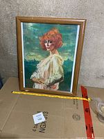 Framed art print featuring a red-haired woman in a pale dress, measuring approximately 18x22 inches, displayed against a neutral background.