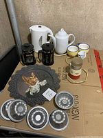 Photo of tea and coffee set items on a cardboard surface including kettle, coffee pots, cups, coffee grinder, decorative cat tray, and baking pans