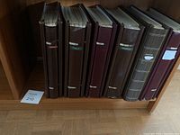 Photo showing a row of seven hardcover photo albums on a wooden shelf. The albums are labeled with country names Denmark, Italy, Switzerland, Greece, and France.