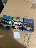 All three DVD box sets for the first three seasons of The West Wing, shown side by side on a cardboard surface.