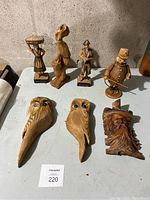 Full view of the lot including 8 diverse folk art wood carvings on a table against wall.