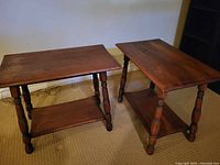 Photo showing two matching antique wooden side tables with turned legs and lower shelves, placed side by side on carpet.