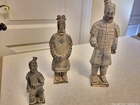 Frontal view of 3 ceramic Terra Cotta Warrior replica figures standing side by side on table.