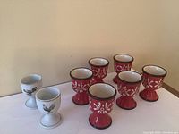 Eight ceramic egg cup holders displayed together showing two different designs and colors.