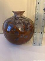 Front side view of the round, brown-tone art pottery vase with blue-gray floral leaf patterns next to a ruler for size reference.