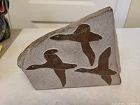 Oblique front view of marble slab showing three Canada geese in bas-relief with artist's signature visible on one goose.