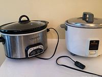 Side-by-side photo of the Crock Pot slow cooker (stainless steel and black) and National rice cooker (white with metal lid and grey handle).