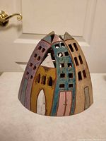 Single close-up photo of the ceramic candle cover shaped like a grouping of houses with painted doors and windows.