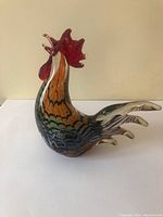 Glass rooster sculpture photographed from front left angle showing body colors and red comb.