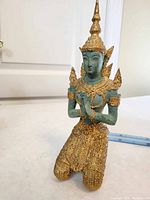 Front view of a kneeling praying figure with green patina and gold painted details, measuring about 21 cm tall.