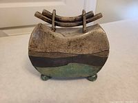 Front view of the raku ceramic box showing glaze colors, curved shape, bow handle on lid, and ball feet at the base.